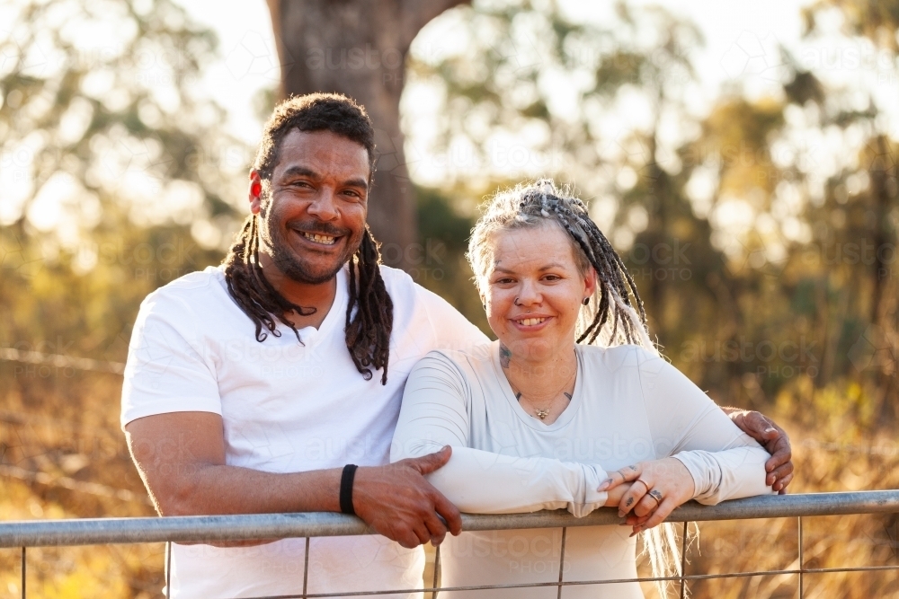 Happy aboriginal Australian couple leaning on farm gate together in country - Australian Stock Image