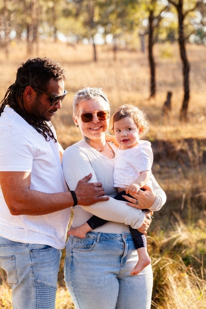 Happy aboriginal family mum, dad and baby girl standing together - Australian Stock Image