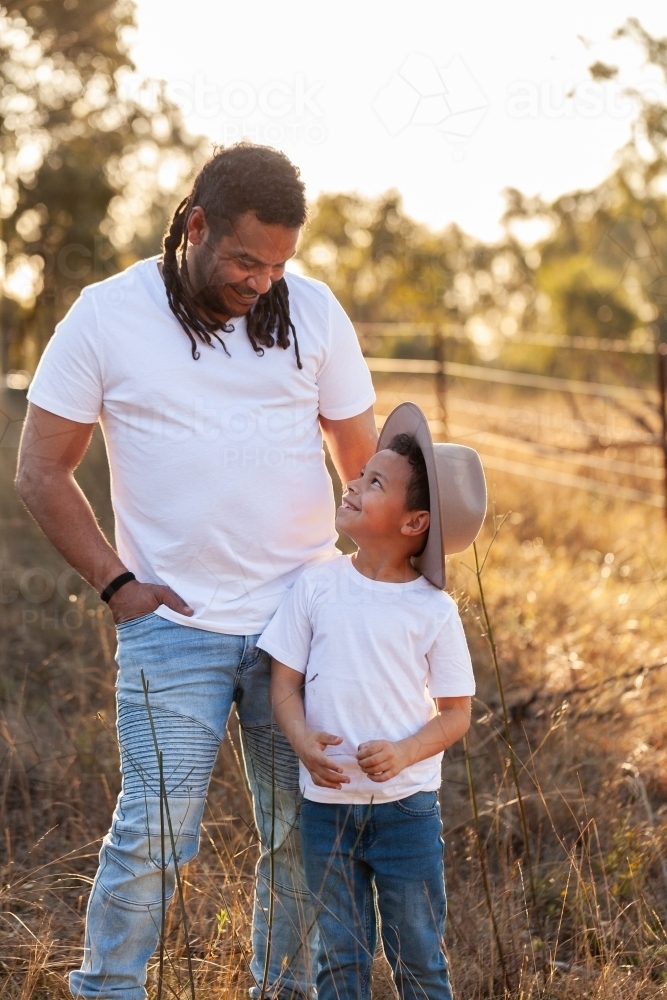 Happy aboriginal father with son in paddock smiling together - Australian Stock Image