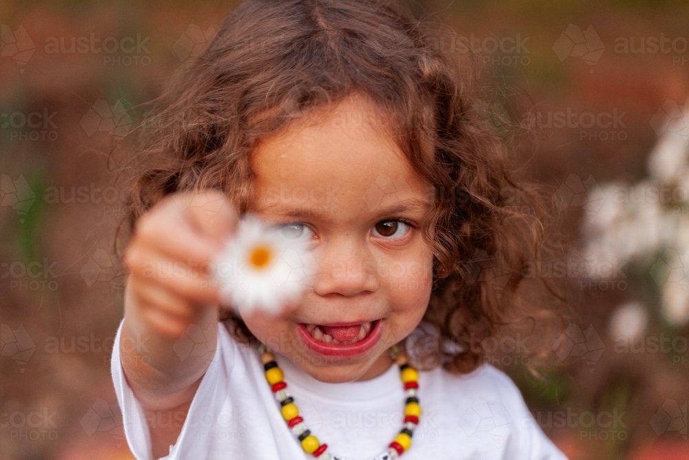 Happy aboriginal girl holding out daisy towards the camera - Australian Stock Image