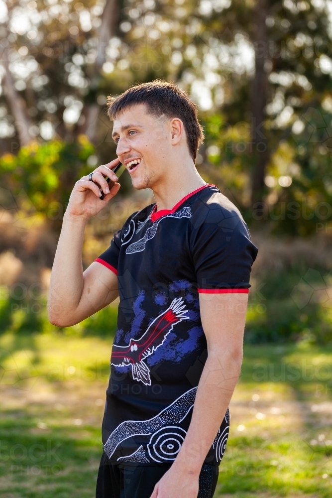 Happy aboriginal teenager in sports polo talking on mobile phone - Australian Stock Image