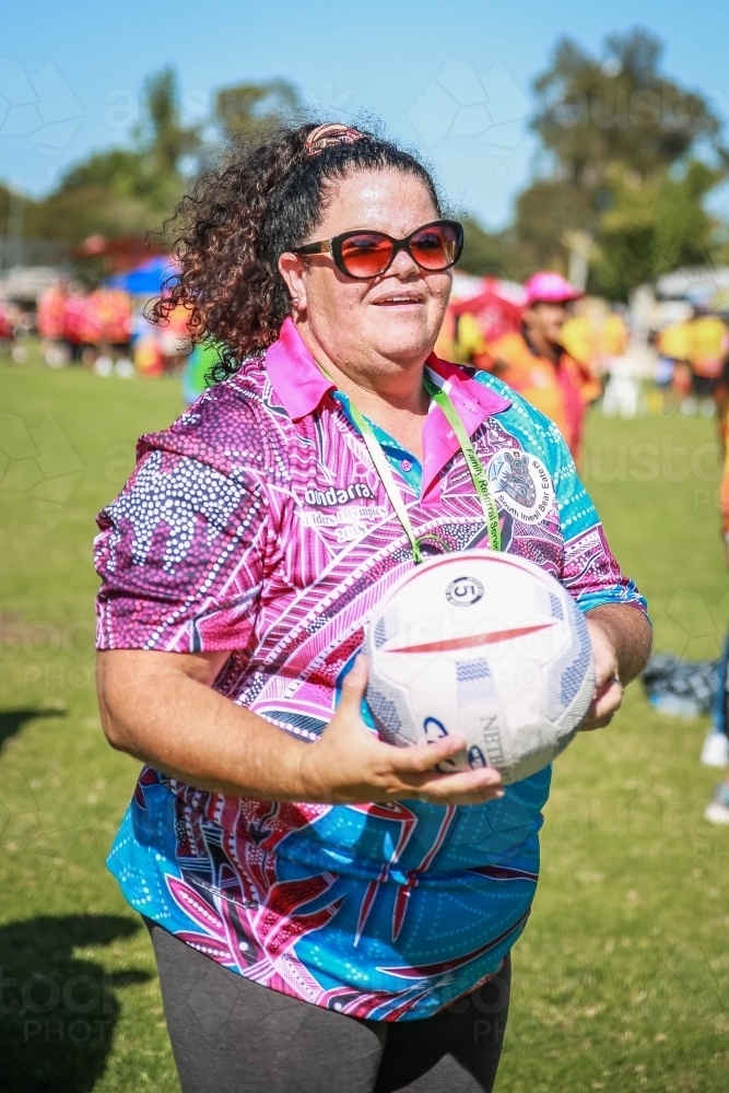 Happy Aboriginal woman with glasses holding netball - Australian Stock Image