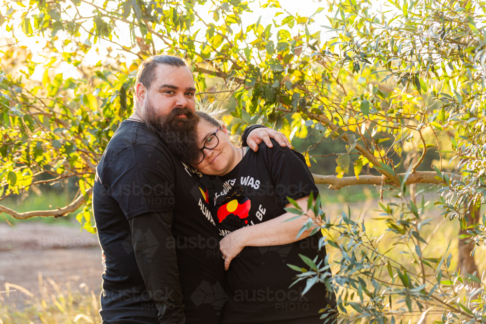 Happy aboriginal Worimi couple hug in bushland wearing always was always will be t shirt - Australian Stock Image