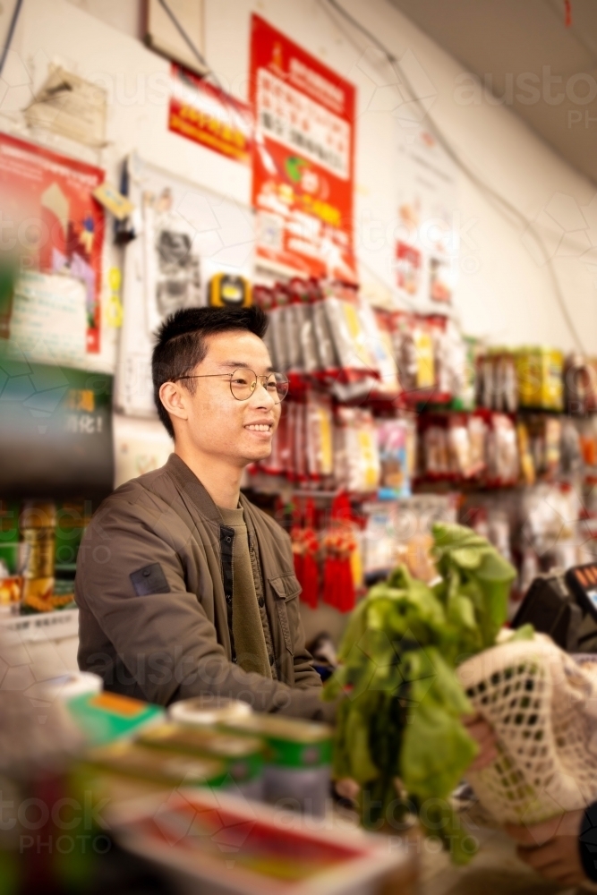 Happy Asian grocery store manager in Ashfield working at the counter - Australian Stock Image