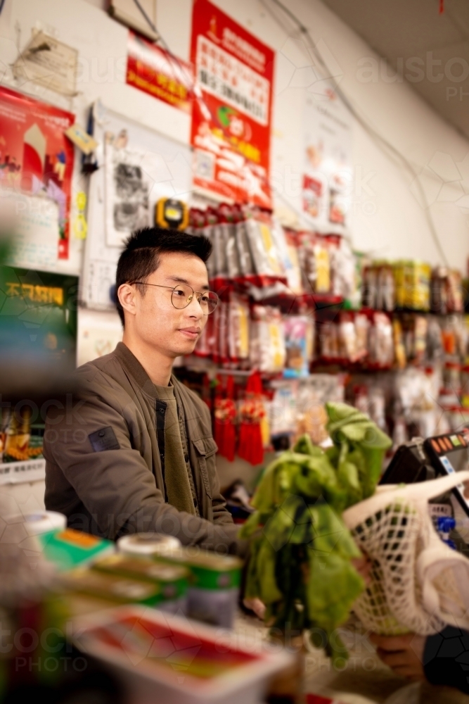 Happy Asian grocery store manager in Ashfield working at the counter - Australian Stock Image