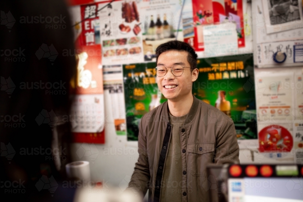 Happy Asian grocery store manager in Ashfield working at the counter - Australian Stock Image