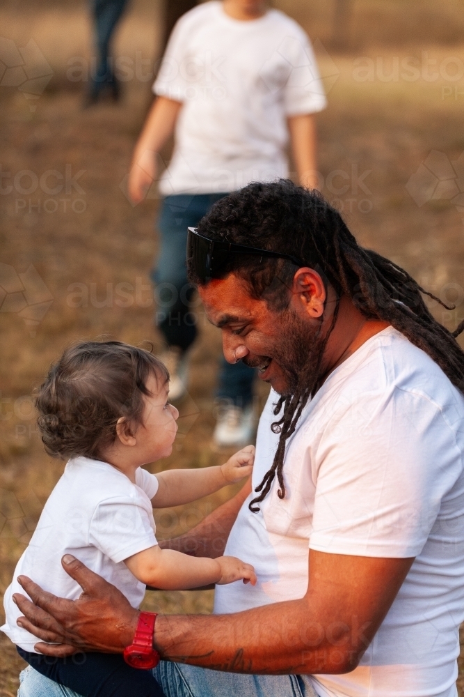 Happy Aussie baby girl with aboriginal father smiling together in soft sunset light - Australian Stock Image