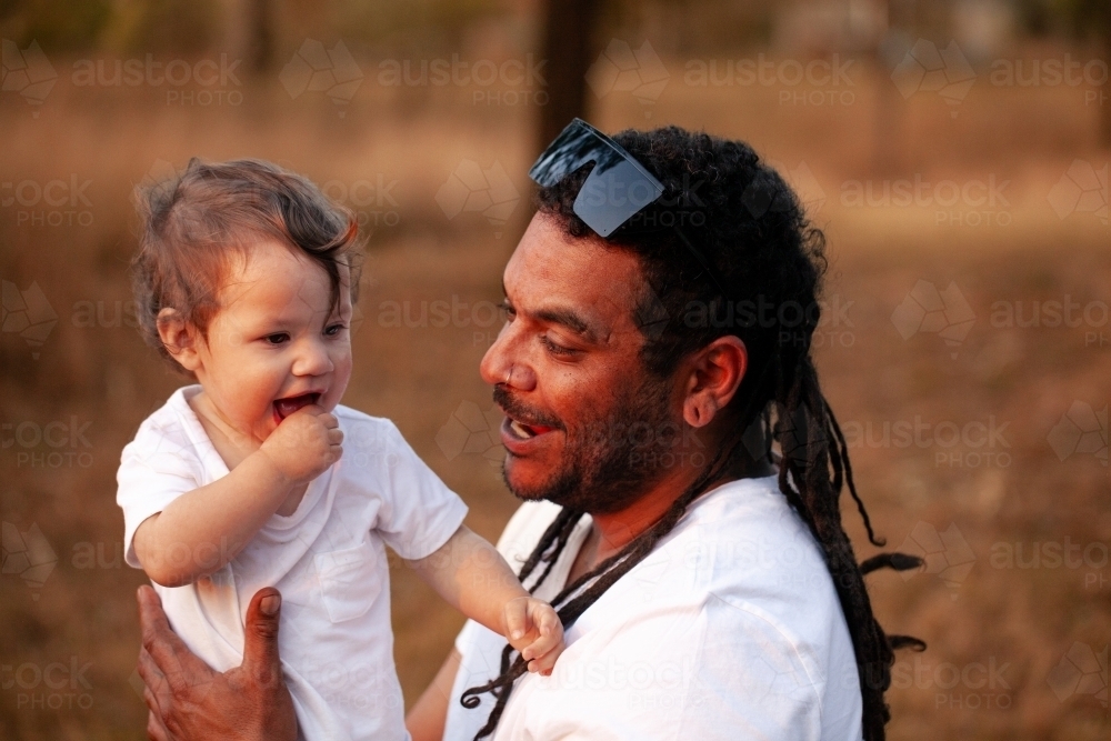 Happy Aussie baby girl with aboriginal father smiling together in soft sunset light - Australian Stock Image