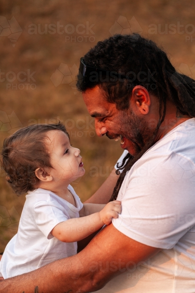 Happy Aussie baby girl with aboriginal father smiling together in soft sunset light - Australian Stock Image