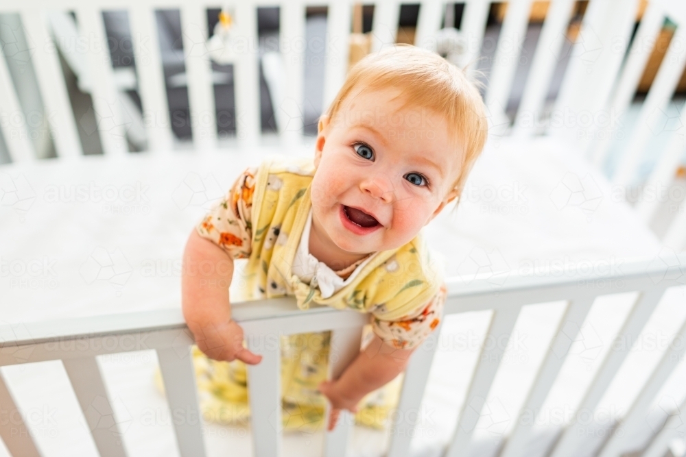 Happy aussie baby smiling up at camera from cot in bedroom - Australian Stock Image