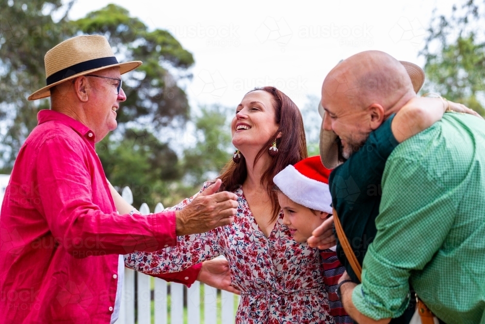 Happy Aussie family of multiple generations greeting one another with hugs at Christmastime - Australian Stock Image