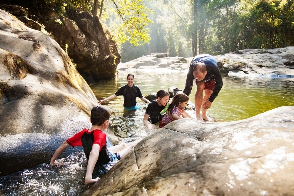 Happy Aussie family with young kids playing in cool water of creek in summer - Australian Stock Image