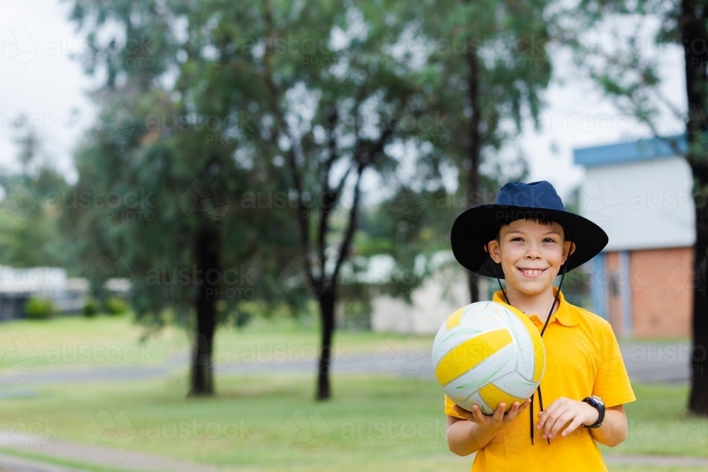 Happy Aussie school boy holding ball to play sports at school - Australian Stock Image