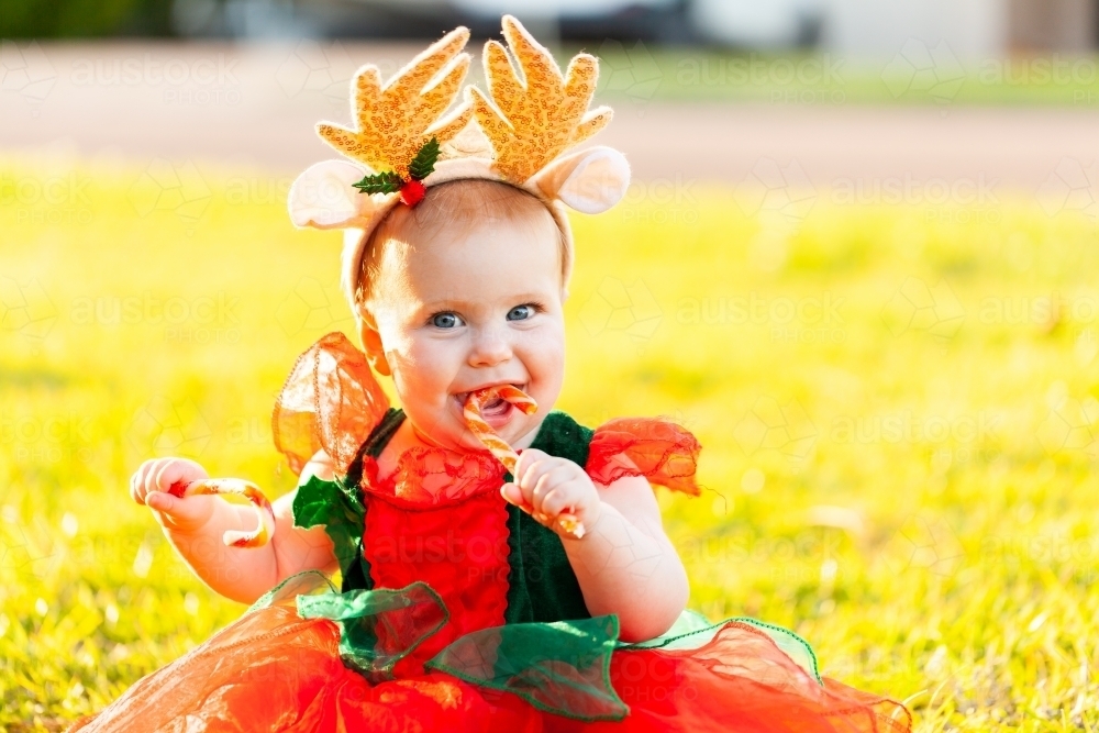 Happy baby at first Christmas wearing reindeer antler and playing with candycanes - Australian Stock Image