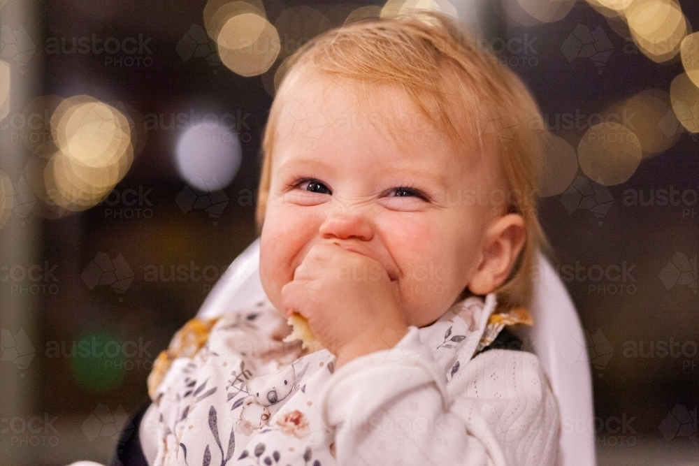 Happy baby eating food at a restaurant smiling at camera late night out - Australian Stock Image