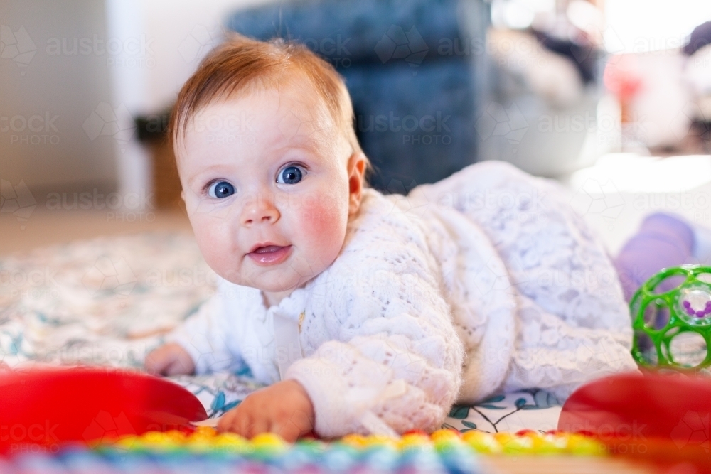 Happy baby girl with bright blue eyes playing with colourful abacus beads - Australian Stock Image