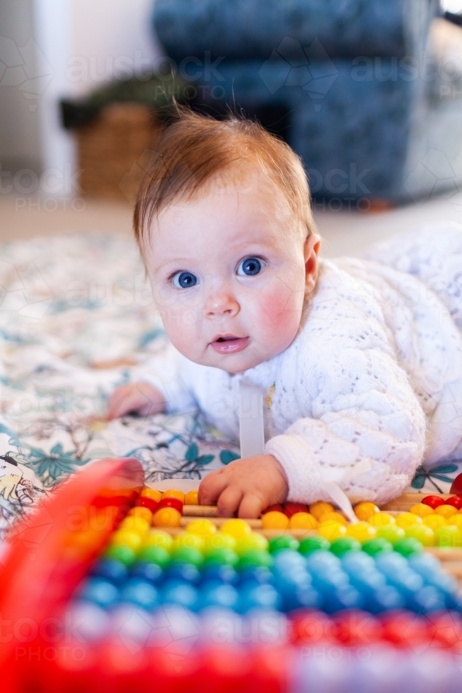 Happy baby girl with bright blue eyes playing with colourful abacus beads - Australian Stock Image