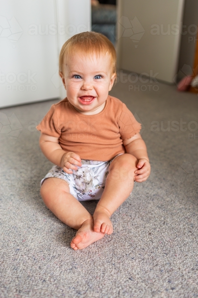 Happy baby sitting up on the floor in home - Australian Stock Image