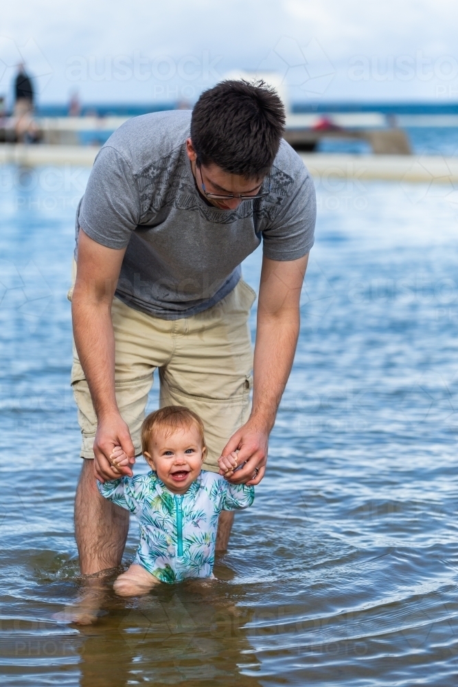 Happy baby walking through sea water in ocean pool at first trip to the beach - Australian Stock Image