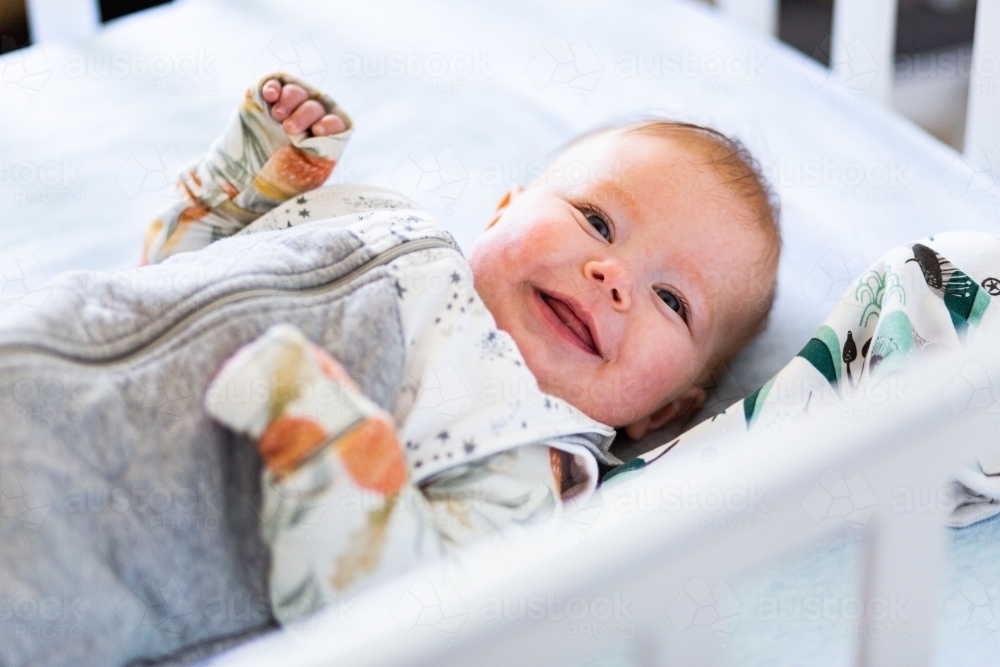 Happy baby with arms out sleep suit smiling in morning - Australian Stock Image