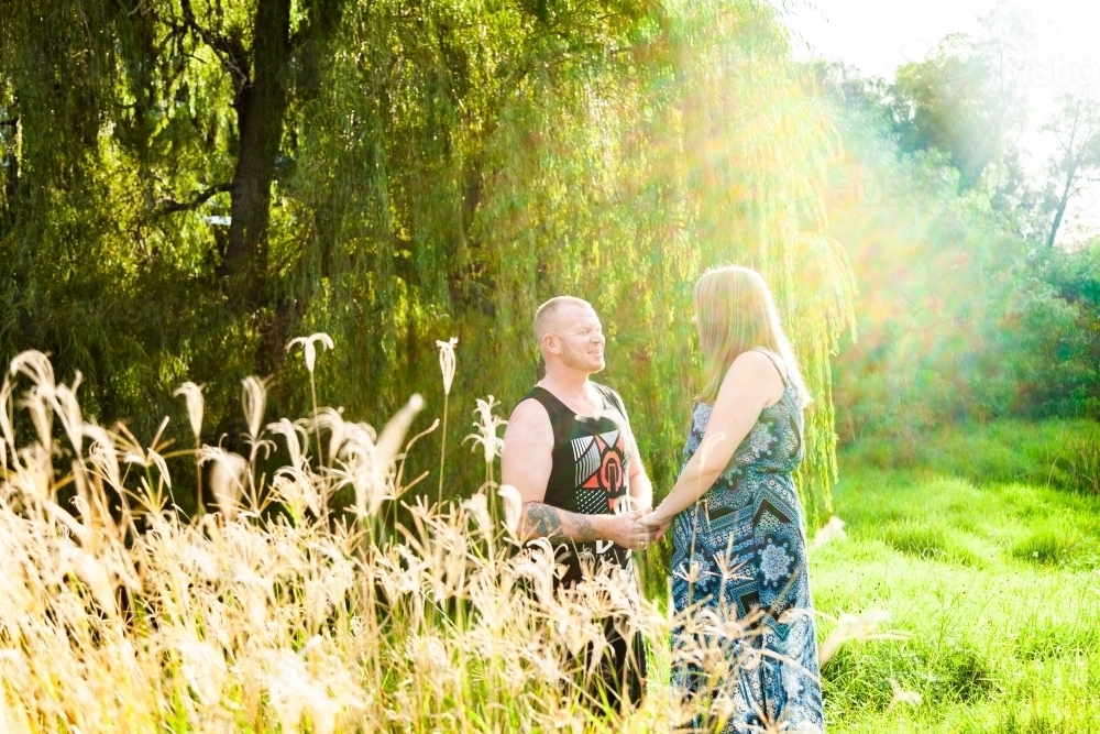 Happy backlit couple standing together in long grass - Australian Stock Image