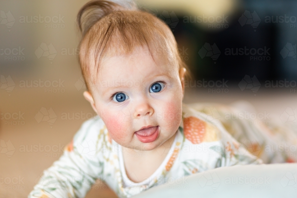 happy blue eyed baby close up playing on floor - Australian Stock Image