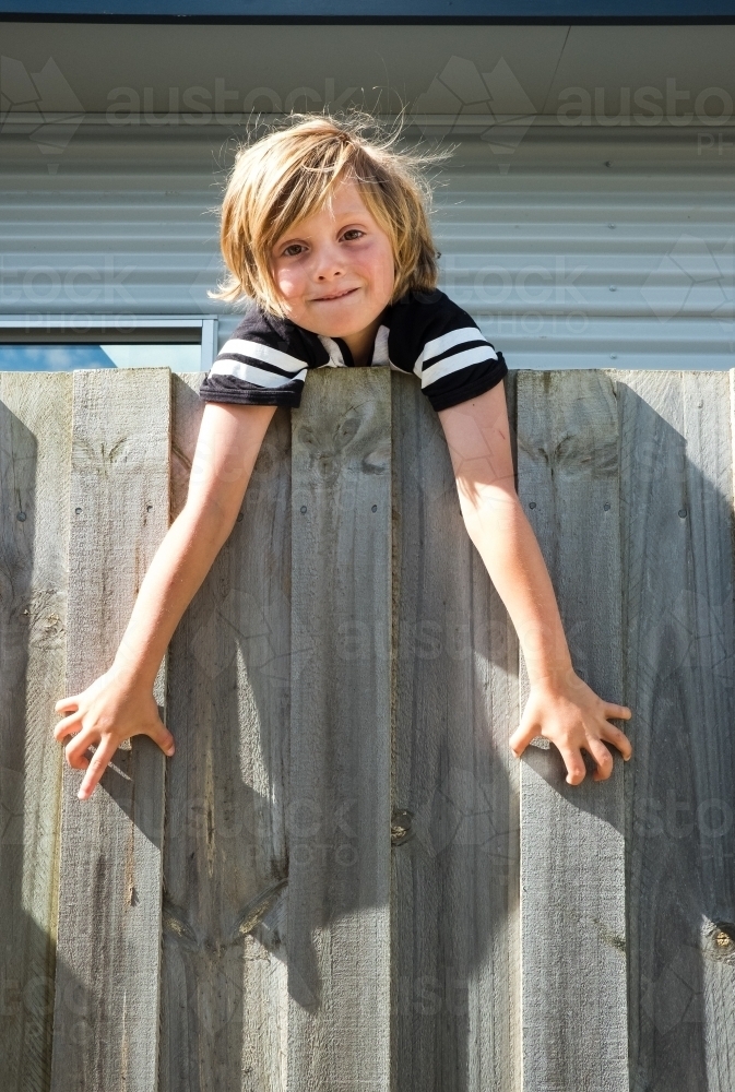 Happy boy hangs over the fence. - Australian Stock Image