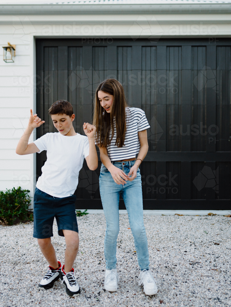 Happy brother and teen sister being silly together outside carport at home - Australian Stock Image