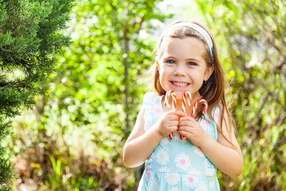 Happy child holding up candy canes outside - Australian Stock Image