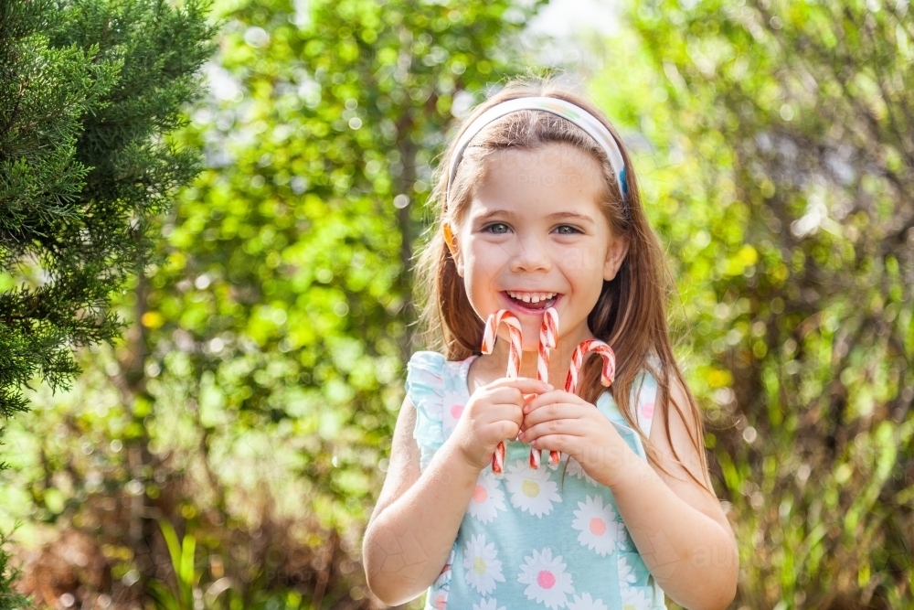 Happy child holding up candy canes outside - Australian Stock Image