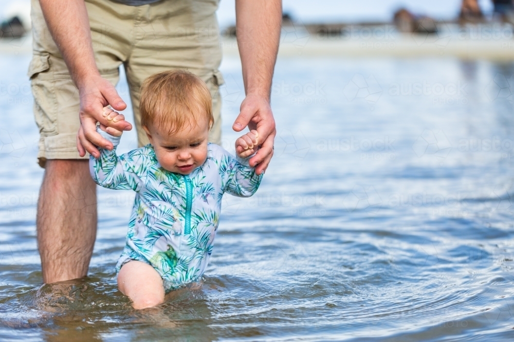 Happy child with dad in sea water in ocean pool at first trip to the beach with parent - Australian Stock Image