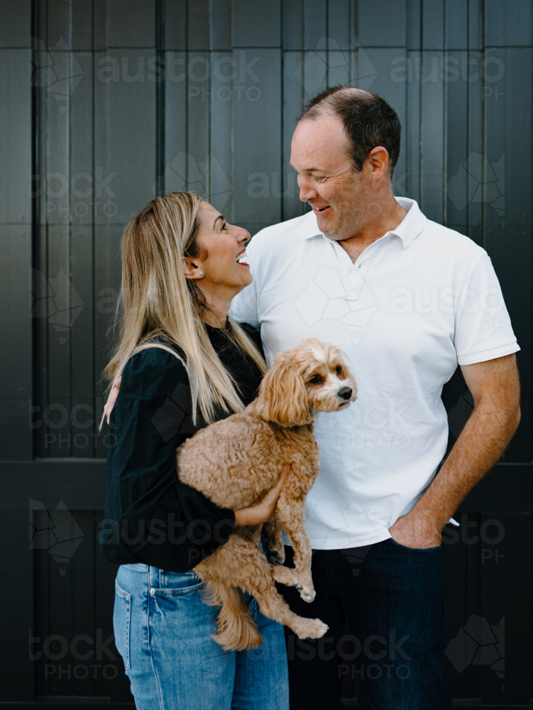 Happy couple looking at each other lovingly holding pet dog - Australian Stock Image