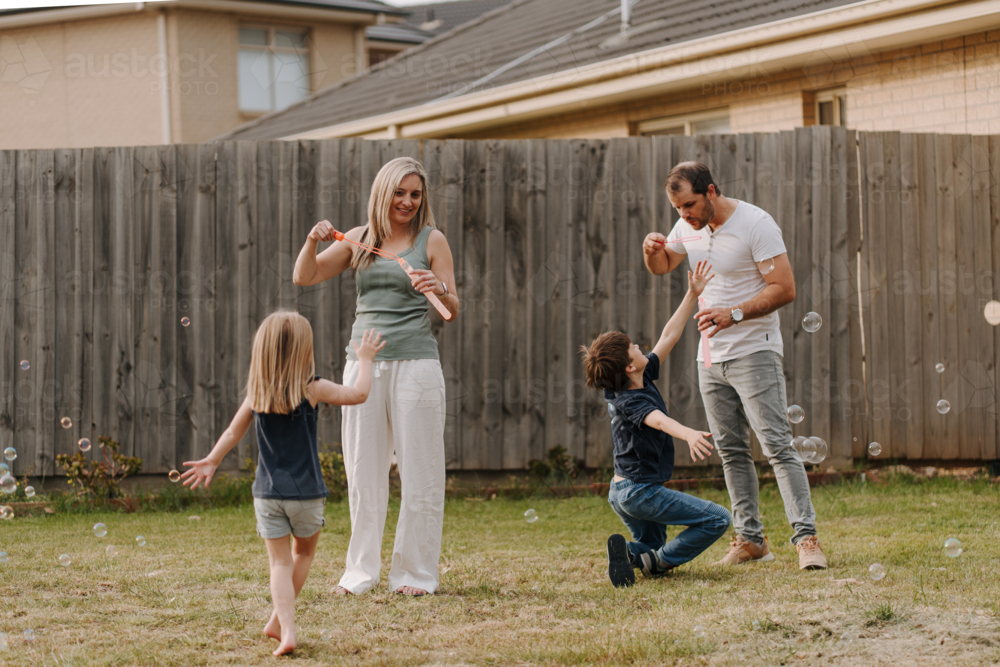 Happy family blowing and playing with bubbles in their yard. - Australian Stock Image