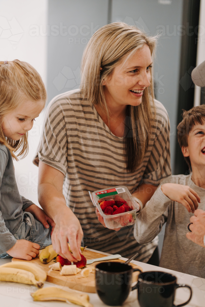 Happy family helping each other prepare food in the kitchen. - Australian Stock Image