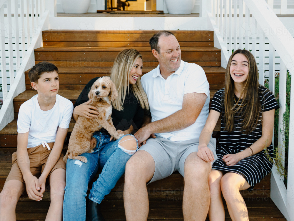 Happy family sitting outside on the steps of their house. - Australian Stock Image