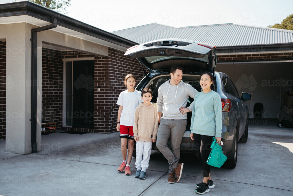 Happy family standing behind the car parked in the driveway - Australian Stock Image