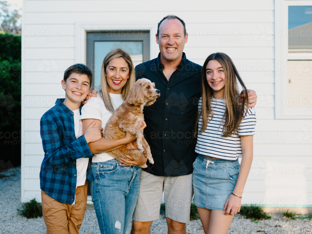 Happy family standing outside their home with their dog. - Australian Stock Image