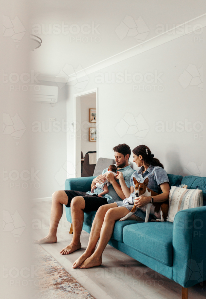 Happy family with newborn baby sitting on the lounge - Australian Stock Image