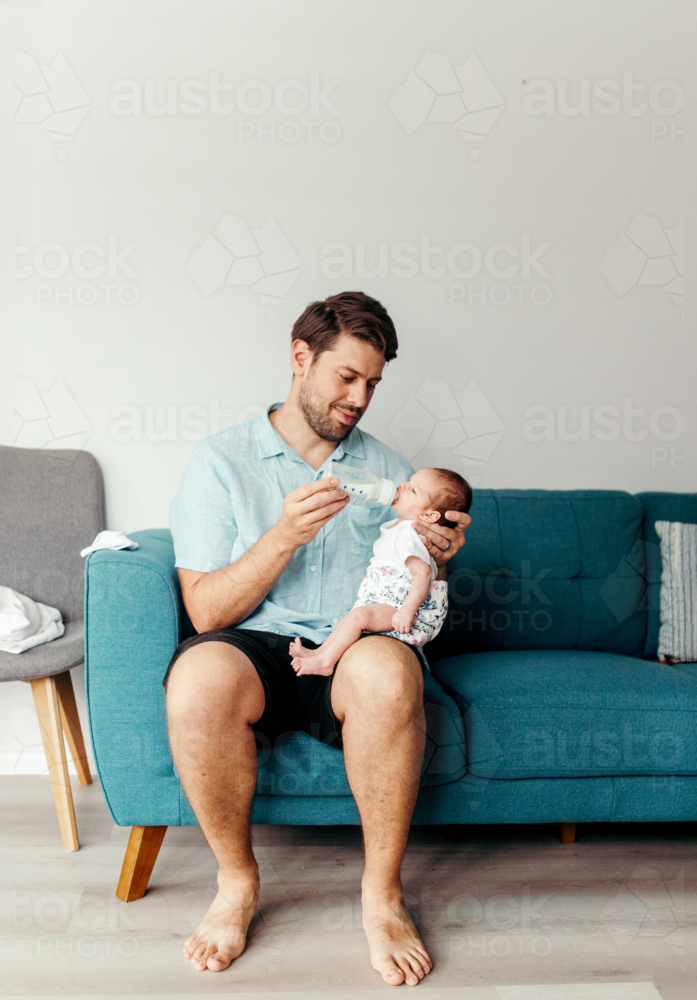 Happy father bottle feeding newborn daughter - Australian Stock Image