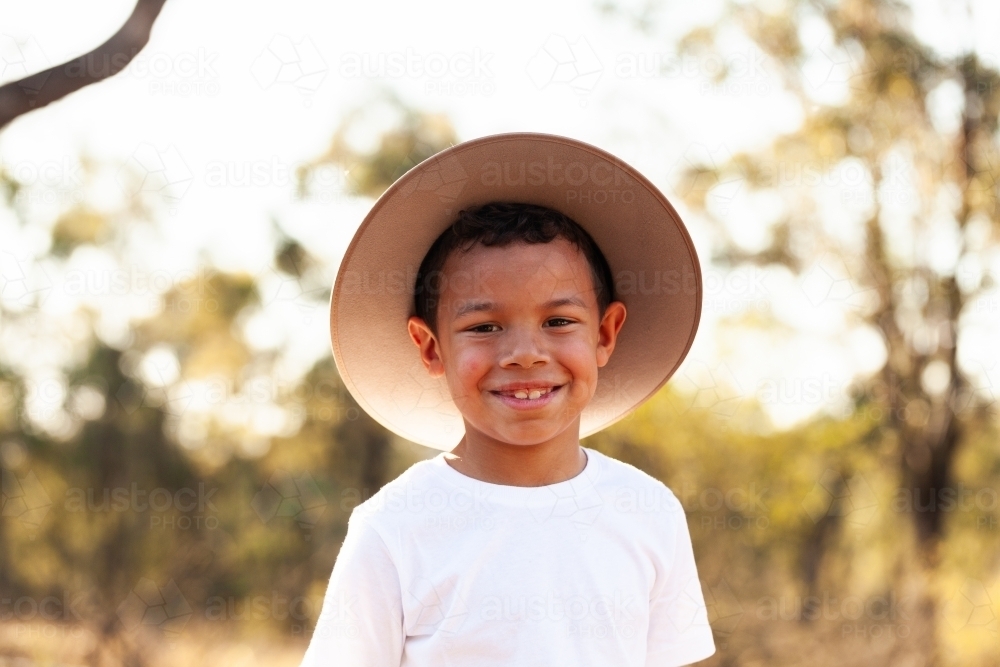 Happy first nations australian kid in country setting wearing hat - Australian Stock Image