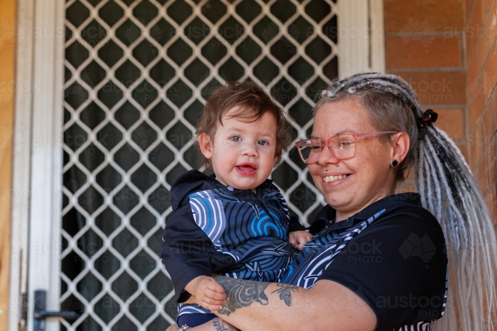 Happy First Nations Australian mum with baby girl by door of home - Australian Stock Image