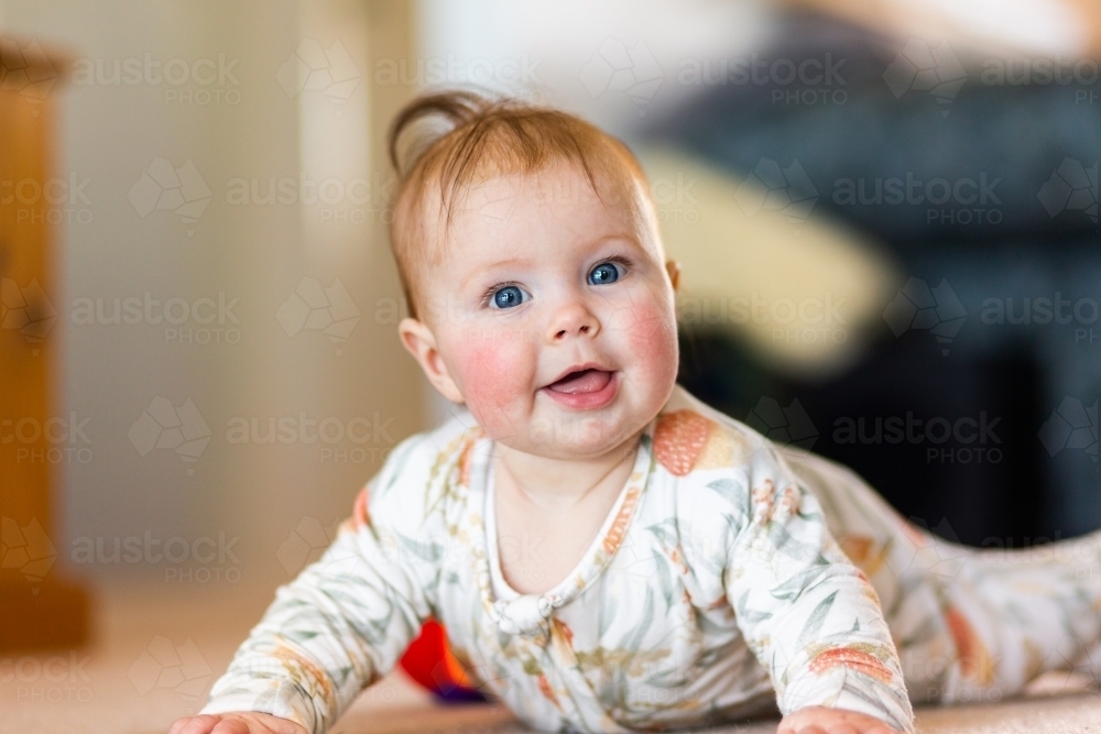 happy five month old baby girl with blue eyes learning to crawl on floor - Australian Stock Image