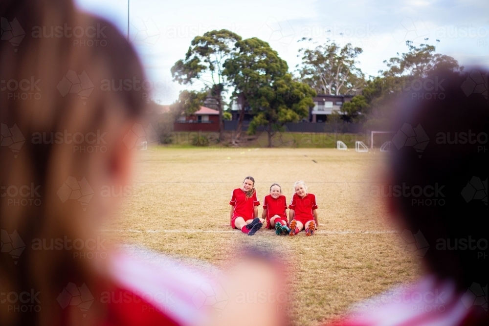 Happy girls wearing red soccer uniforms sitting on the grass together - Australian Stock Image