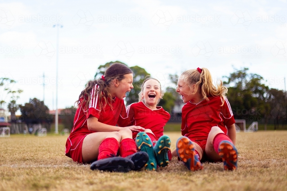 Happy girls wearing red soccer uniforms sitting on the grass together - Australian Stock Image