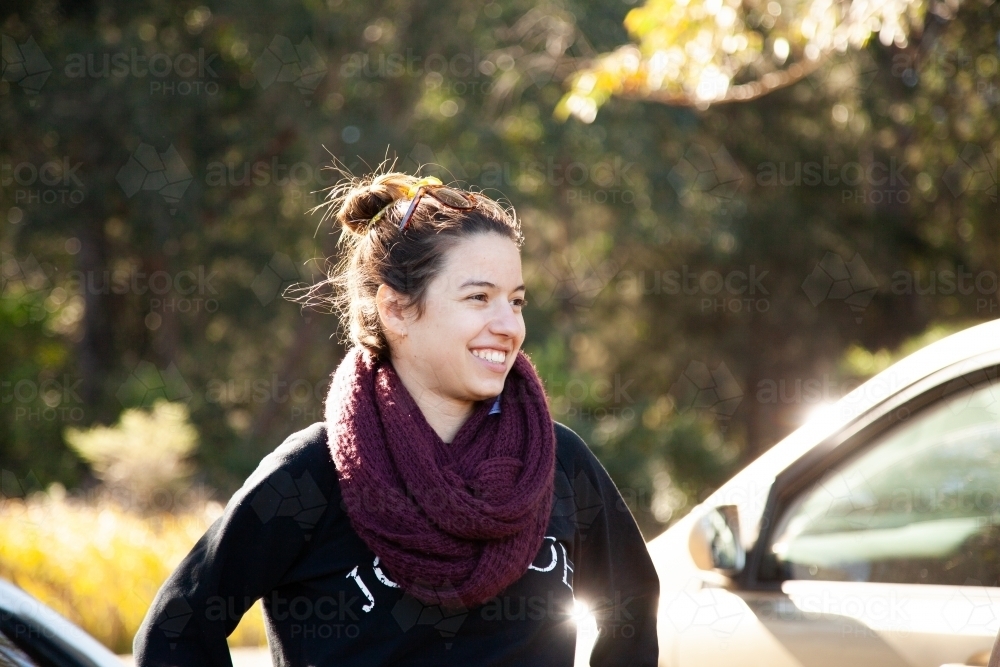 Happy laughing young woman wearing scarf in winter beside car - Australian Stock Image