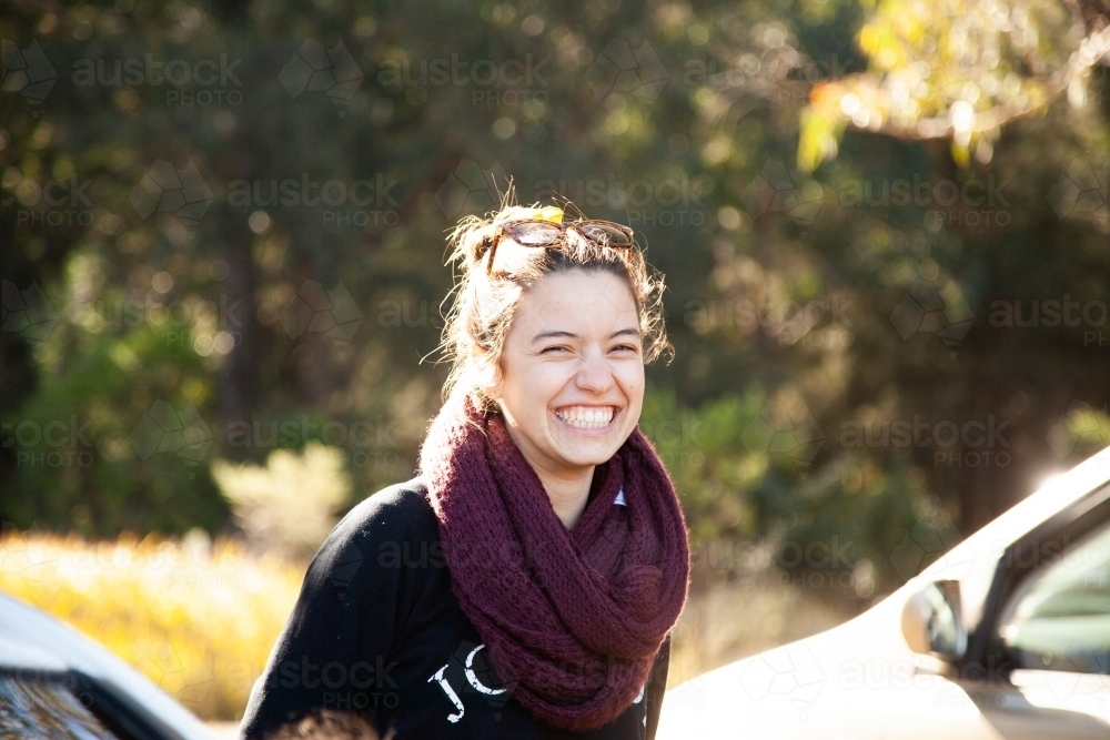 Happy laughing young woman wearing scarf in winter beside car - Australian Stock Image