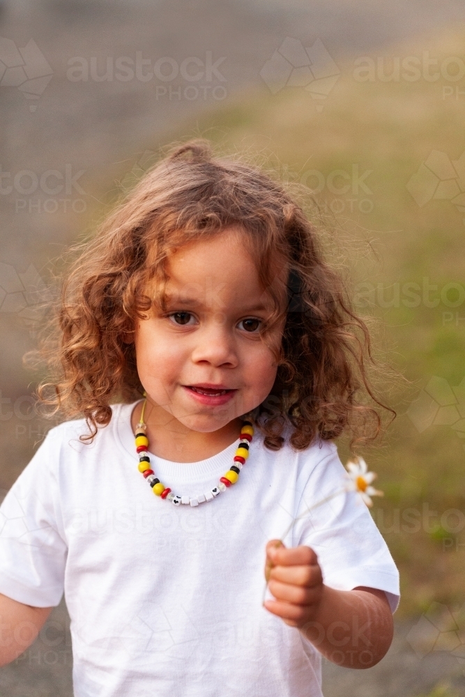 Happy little Aboriginal girl with picked daisy flower at dusk - Australian Stock Image