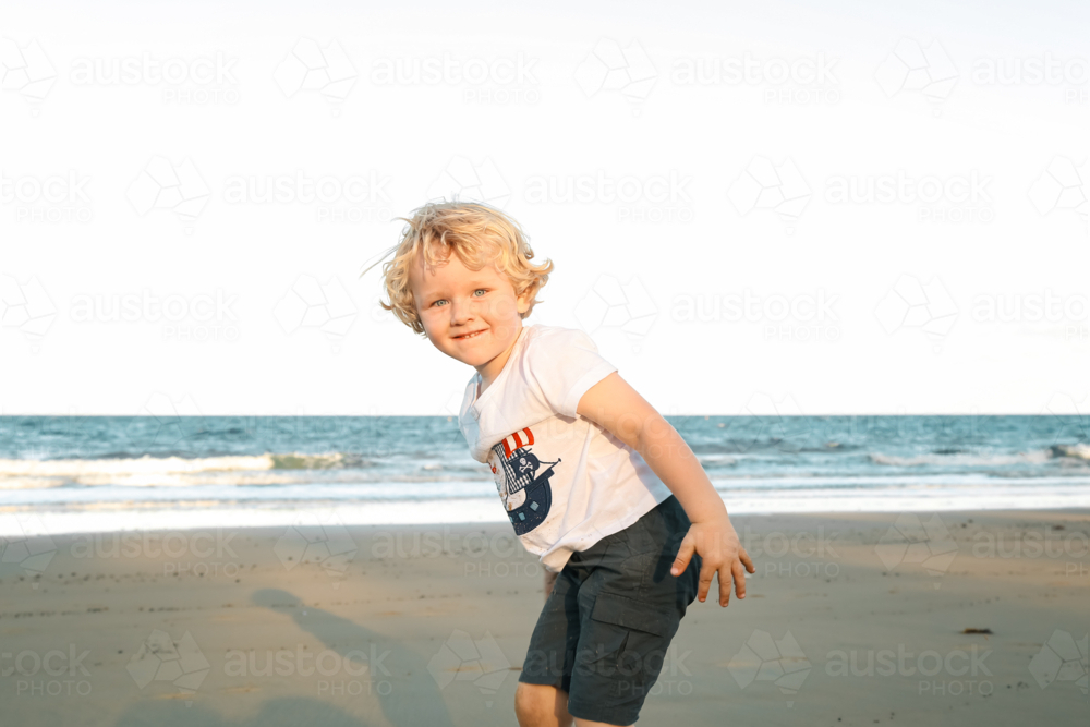 Happy little boy bathed in golden sunshine on the beach - Australian Stock Image
