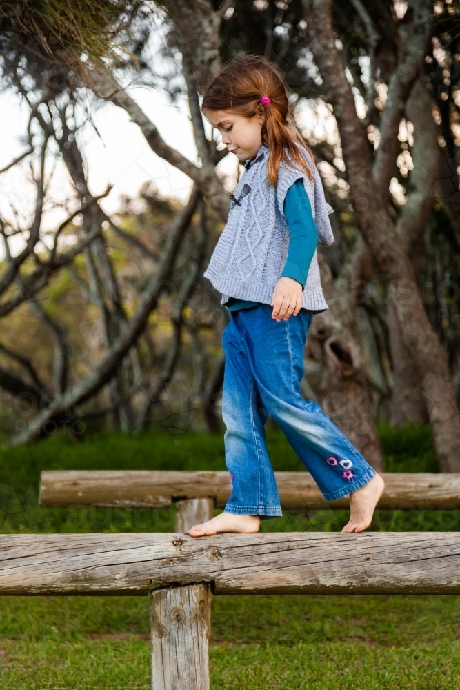 Happy little girl balancing on a pole outside near forest - Australian Stock Image