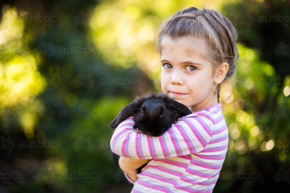 Happy little girl cuddling black pet bunny rabbit - Australian Stock Image